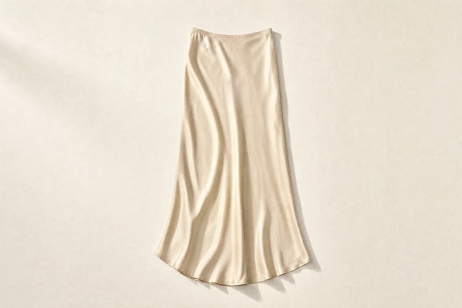 A single silk skirt laid flat and alone on a warm paper surface, photographed from above